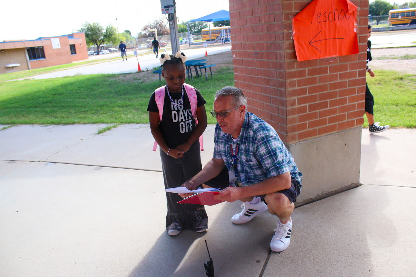 A man crouches down as he helps a girl with her class schedule